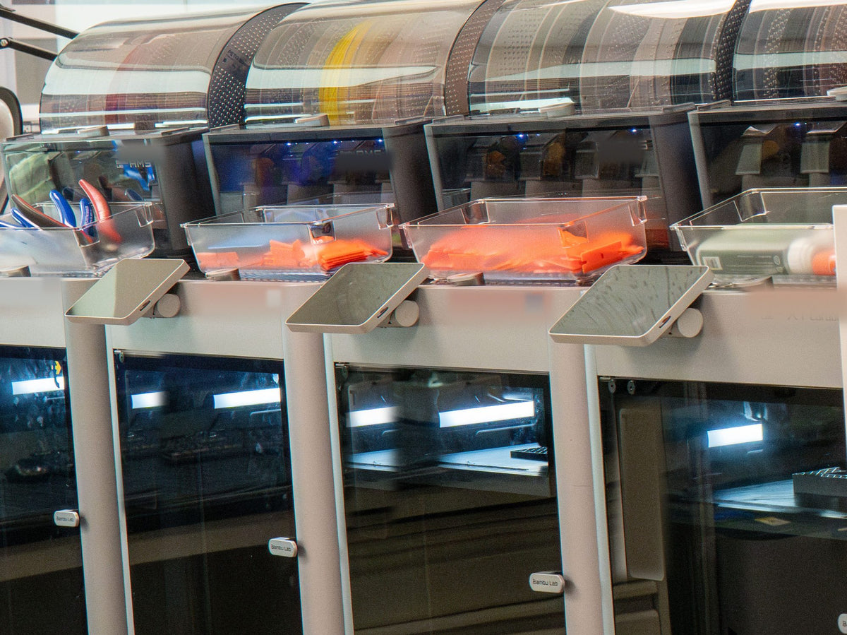 Enclosed 3D printers with trays of printed parts
